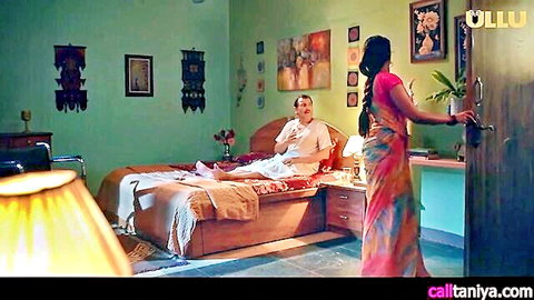 Indian MILF in pink saree stands teasingly by bedroom door as older man lounges on bed watching