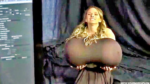 Blonde woman smiling and holding massive photoshop-enhanced breasts in elegant dress