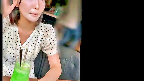 Cute Asian amateur in polka-dot blouse sipping green drink