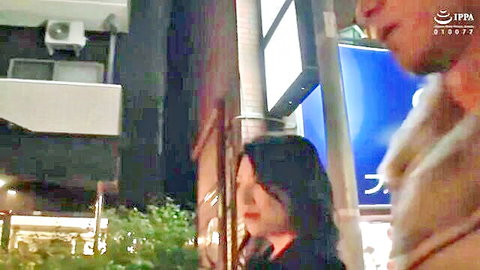 Japanese mature woman with dark hair and red lips stands close to bearded man in neon-lit night alley