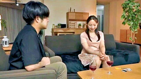 Japanese sister-in-law in pink dress shares wine with brother-in-law on couch