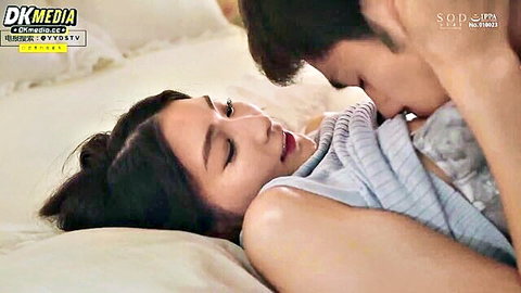 Asian couple passionately kissing on bed with man nuzzling woman's neck