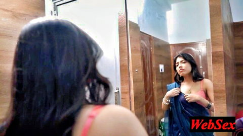 Sexy South Asian babe in pink bra straps trying on blue saree in bathroom mirror
