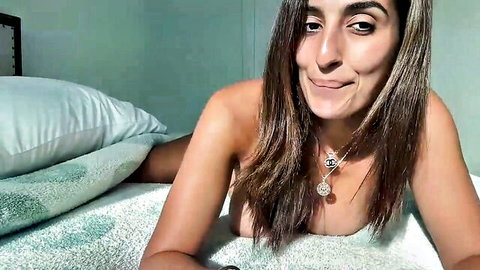 Topless brunette with big tits smiles playfully on bed exposing huge breasts