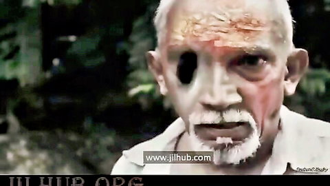 Wounded elderly Sri Lankan man with white beard and red forehead mark stares intensely in jungle scene
