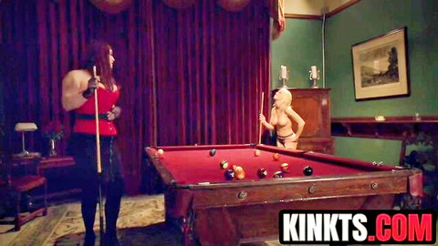 Buff redhead dominatrix in red corset and blonde in skimpy bikini playing pool seductively.