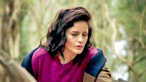 Brunette woman with wavy hair pouting lips in pink sweater and jacket outdoors in forest