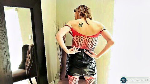 Brunette with tattooed back in red fishnet top and black leather skirt exposing ass cheeks from behind