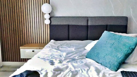 Cozy empty bedroom with gray upholstered headboard, turquoise pillows on messy white sheets and wooden nightstand
