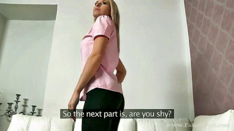 Blonde beauty in pink blouse and black pants posing seductively, teasing 'are you shy?'