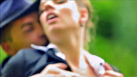 Suited man passionately kisses blonde woman's exposed neck outdoors as she moans in ecstasy