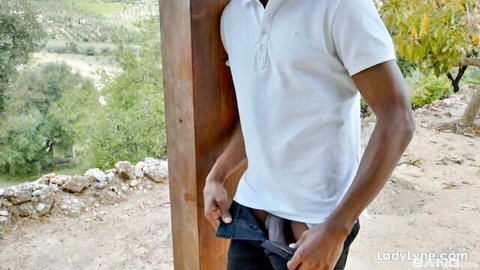 Outdoor ladyboy exposing huge black cock, pulling down pants in white polo shirt