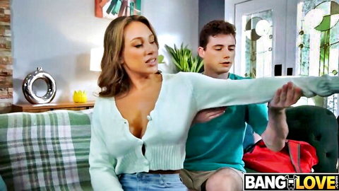 Busty MILF in open cardigan shows deep cleavage teasing young guy on couch