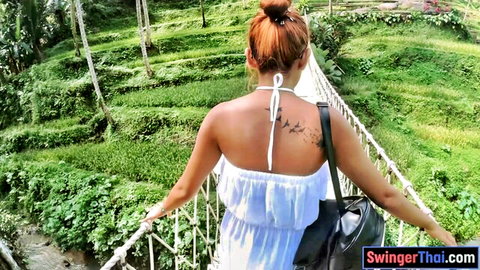 Thai beauty in white dress on scenic bridge, red hair bun, bird tattoo