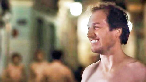 Smiling shirtless hunk in steamy locker room with nude men blurred in background