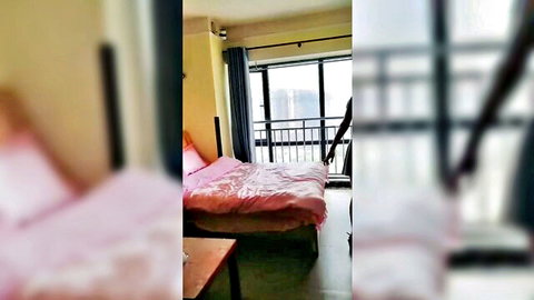 Blurry empty bedroom with pink sheets on bed and balcony window overlooking city