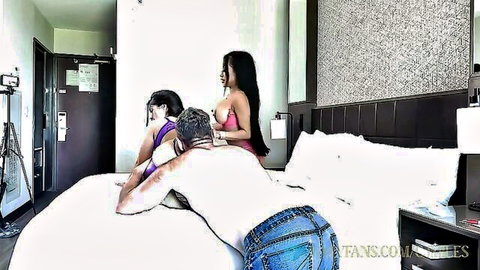 Two busty Asian brunettes in lingerie dominate muscular white guy bent over hotel bed