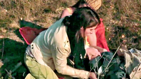 Brunette woman in white top grabs crotch bulge through camo pants outdoors with friends on picnic blanket