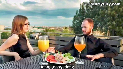 Redhead woman in black dress and bearded man enjoy romantic outdoor dinner with orange juice and salmon salad