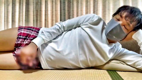 Masked Asian stud in plaid shorts, hand on blurred crotch, lying relaxed solo milking tease
