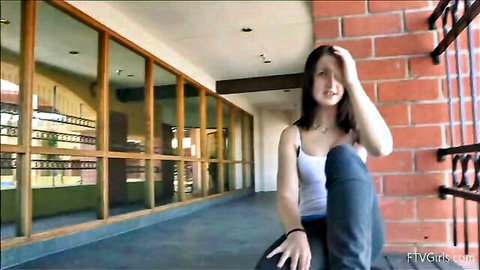 Lean brunette teen sitting casually in white tank top and jeans, looking frustrated