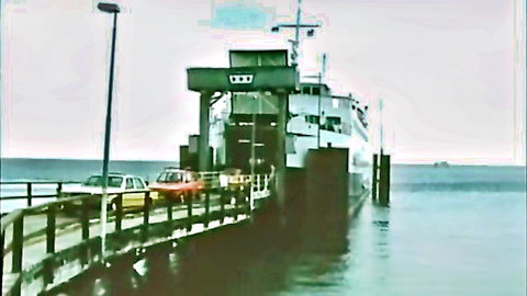 Vintage ferry boat at dock with cars loading, serene waterfront scene from retro video
