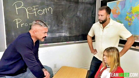 Blonde schoolgirl in uniform surrounded by two men in classroom threesome tease