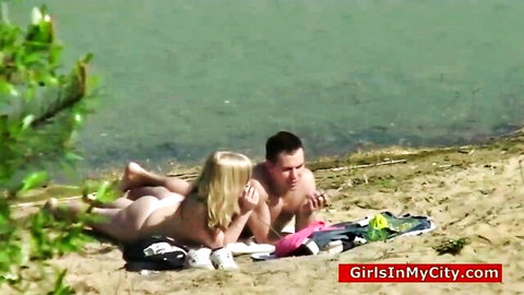Topless blonde in tiny thong exposes bare ass on public beach with guy caressing her