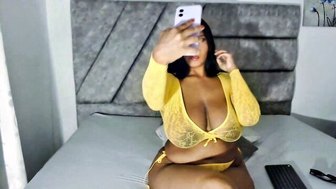 Curvy brunette babe with massive tits in sheer yellow lace lingerie takes webcam selfie on bed