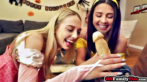 Blonde and brunette Halloween costumed teens laugh holding massive yellow dildo cock.
