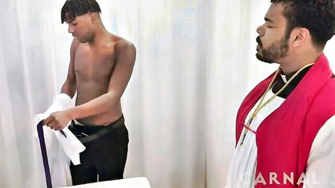 Shirtless Black twink holding towel near robed priest in intimate gay scene