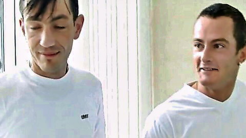 Two young men in white shirts smiling intimately at each other close-up