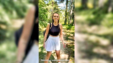 Youthful French girl in black crop top and white pleated skirt walking smiling in forest