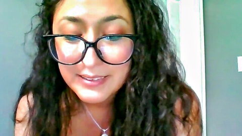 Cute ebony girl with curly hair and black glasses smiling seductively on webcam