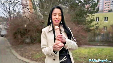 Brunette babe in trench coat holds massive realistic dildo in public park outdoors