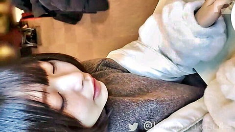 Cute Asian girl with bangs in cozy gray sweater, sleepy eyes closed cuddling fluffy toy