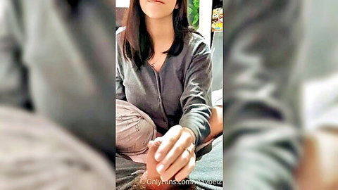 Asian woman in gray sweater teases bare foot with hand, foot fetish vibe