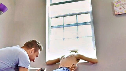 Blonde stepsis leaning out window in jeans, stepbro behind her in casual setup