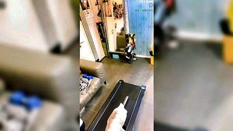Amateur hand gripping thick white dildo on treadmill belt in cluttered home gym.