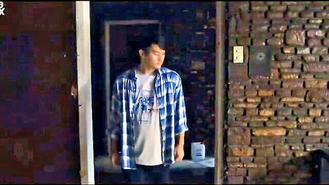 Young Asian man in checkered shirt and jeans standing in dimly lit doorway, Vivamax adult scene