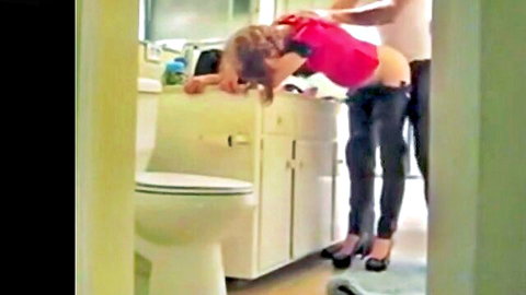 Blonde wife bent over sink, pants down exposing ass, man behind in cheating scene