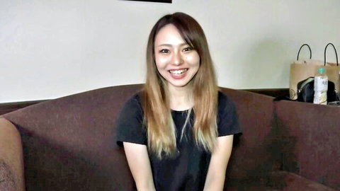 Cute Japanese girl with long blonde-tipped hair smiling happily on couch in black t-shirt
