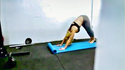 Blonde fitness babe in downward dog yoga pose, sports bra and tight leggings