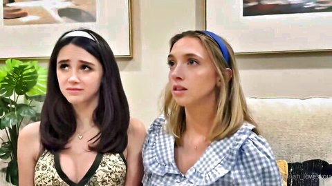 Two busty teens in low-cut tops showing deep cleavage sitting surprised on couch