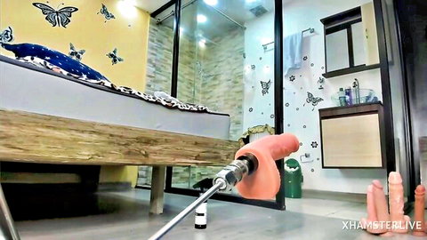 Large pink dildo on metal fucking machine in steamy yellow bathroom with butterfly decor and extra cocks
