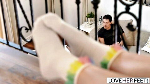 Woman's feet in rainbow-striped socks teased from balcony over man on couch