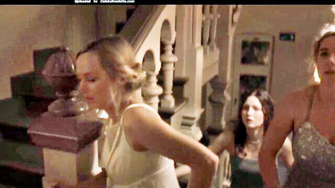 Emotional blonde in white dress with brunettes in gowns on staircase, nude movie scene