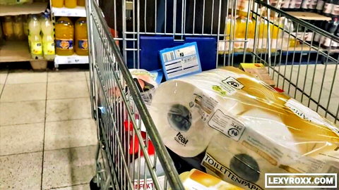 Shopping cart overflowing with toilet paper packs in supermarket aisle with orange juice shelves