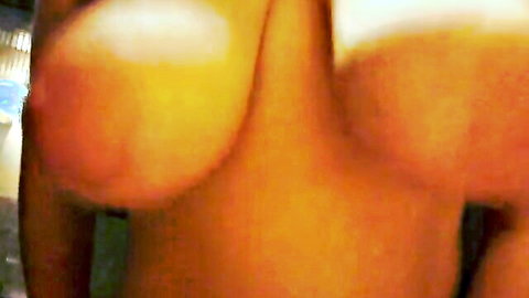 Blurry close-up of massive bare orange-tinted tits squeezed together