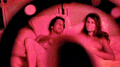 Nude brunette with medium tits lies naked beside muscular man on bed in red fisheye glow